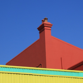 Coloured red roof and yellow and green brick wall against a blue sky